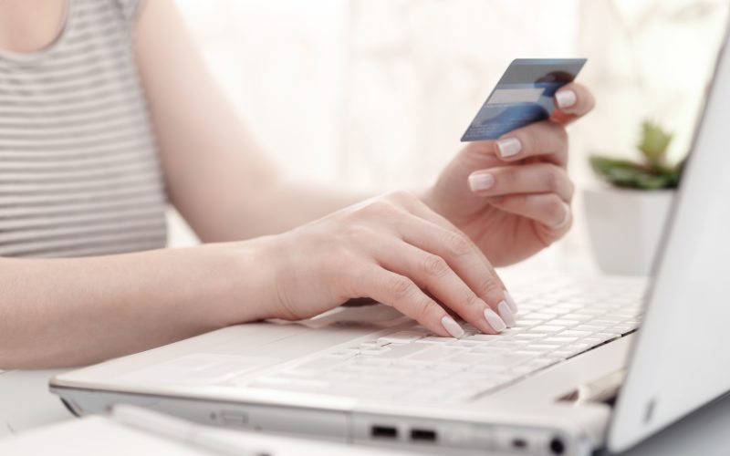 female hands using credit card Close up of female hands using modern computer and credit card, high key. Shopping online